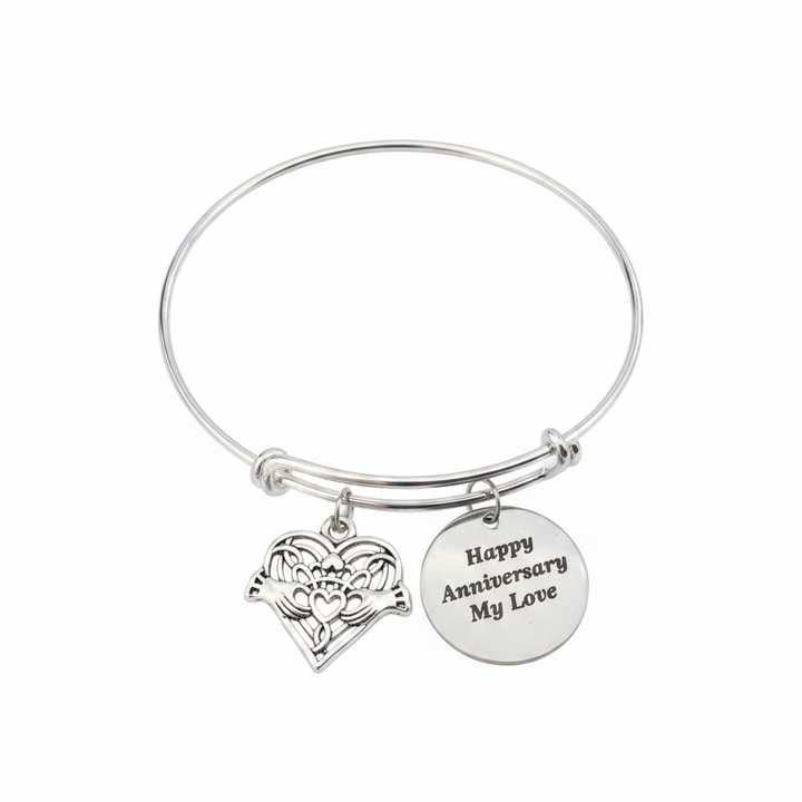 Professional white background studio photo of silver Happy Anniversary My Love bracelet with Claddagh heart filigree charm and engraved round disc charm – romantic anniversary jewelry gift