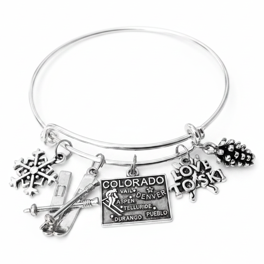 Silver expandable charm bangle bracelet with snowflake charm, ski and poles charm, Colorado engraved tag charm with Vail Denver Aspen Telluride cities, Love to Ski charm, and pine cone charm, handcrafted by Jules Obsession