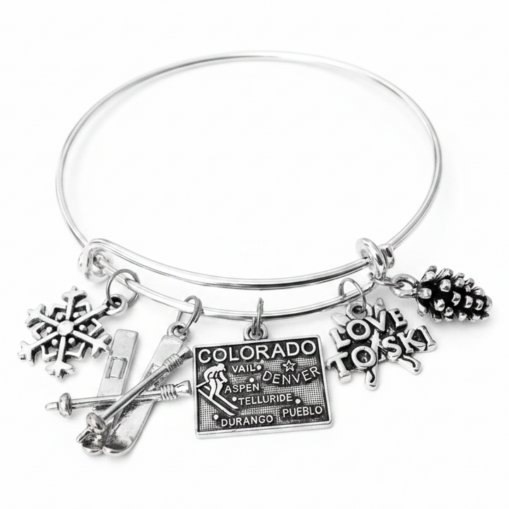 Silver expandable charm bangle bracelet with snowflake charm, ski and poles charm, Colorado engraved tag charm with Vail Denver Aspen Telluride cities, Love to Ski charm, and pine cone charm, handcrafted by Jules Obsession