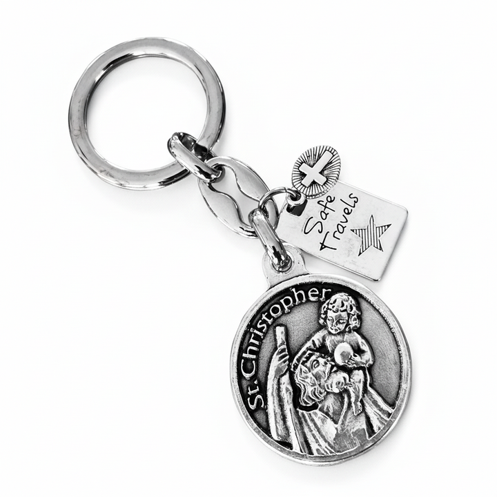 Silver-tone St. Christopher Safe Travels keychain with engraved medal, travel tag, star, and cross charm on white