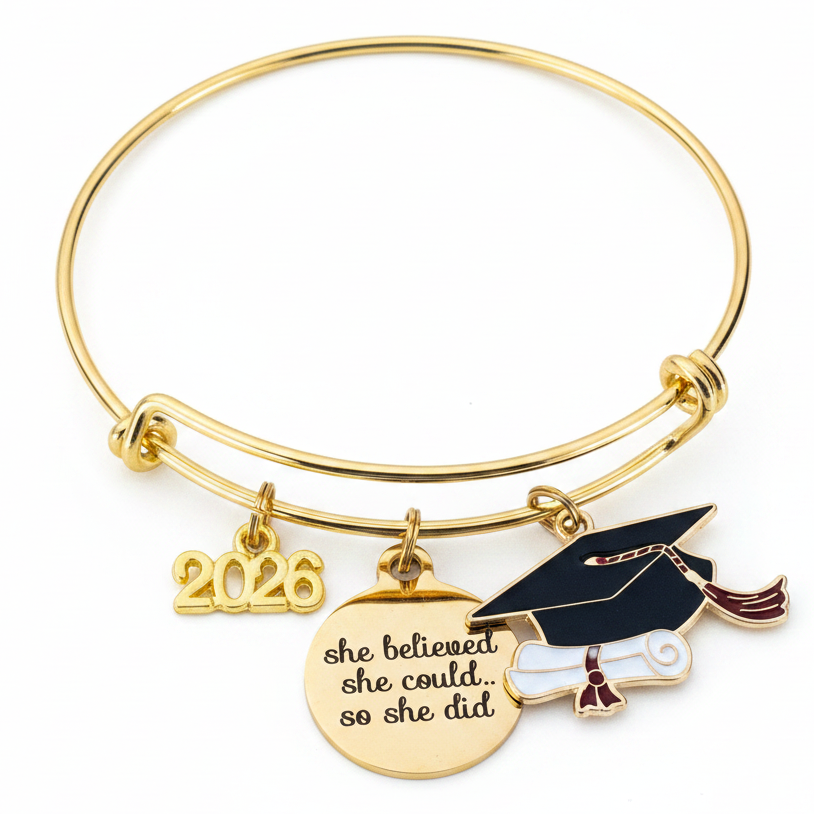 Gold graduation charm bangle bracelet on white background featuring 2026 charm, she believed she could engraved disc, and enamel graduation cap with diploma, professional product photo