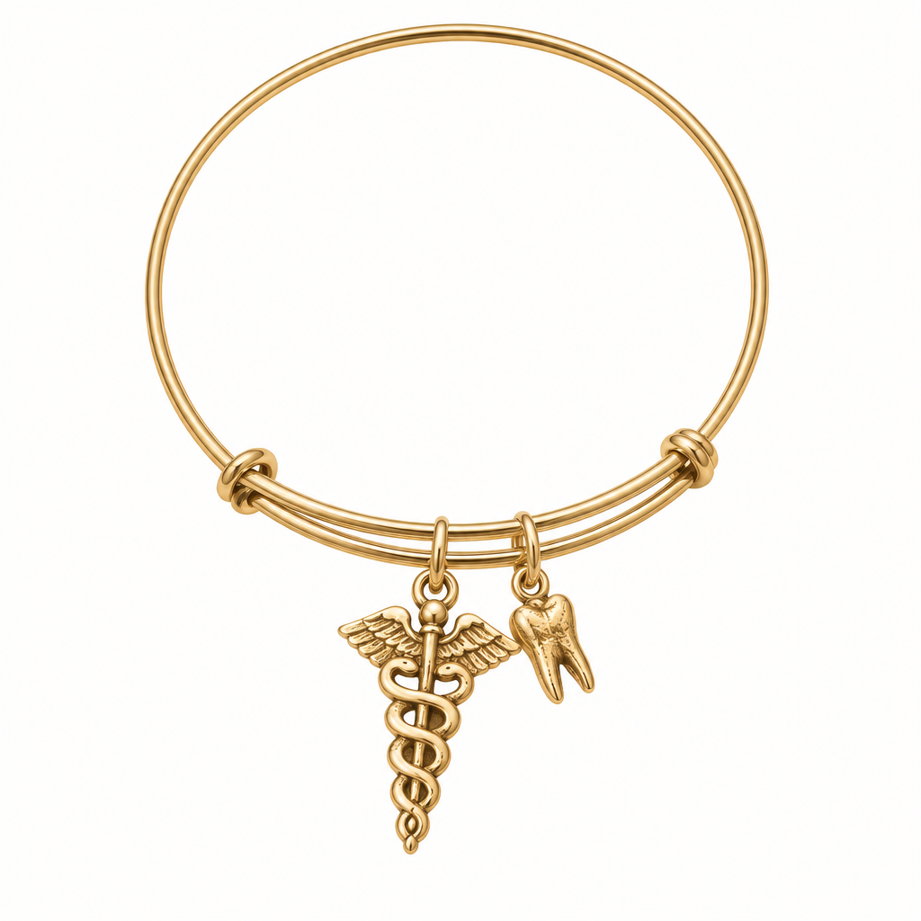 Gold bangle bracelet with a caduceus medical symbol charm and a tooth-shaped charm, shown on a clean warm-white studio background