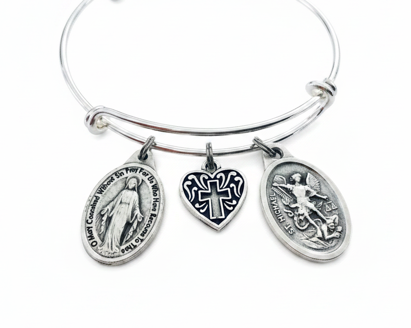 Silver expandable bangle bracelet with three charms: Miraculous Mary oval medallion, black enamel heart cross charm, and St. Michael the Archangel oval medallion, on white background