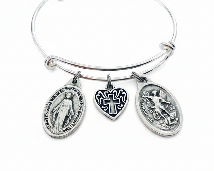 Silver expandable bangle bracelet with three charms: Miraculous Mary oval medallion, black enamel heart cross charm, and St. Michael the Archangel oval medallion, on white background