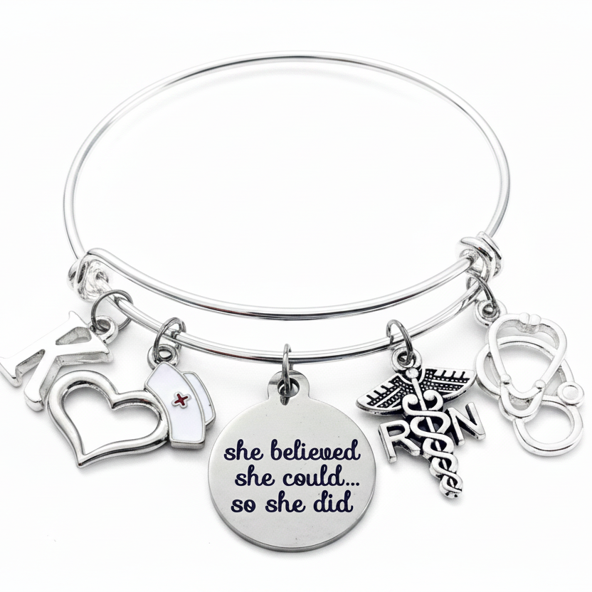 Silver expandable bangle bracelet with nurse-themed charms including RN caduceus, stethoscope, nurse cap, open heart, and inspirational disc charm reading she believed she could so she did, on white background