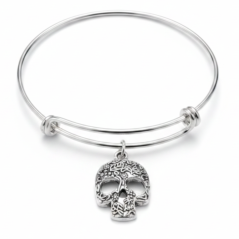 Silver expandable wire bangle bracelet on white background with a large silver sugar skull charm connected by a jump ring, featuring intricate floral and leaf engravings with hollow eye sockets