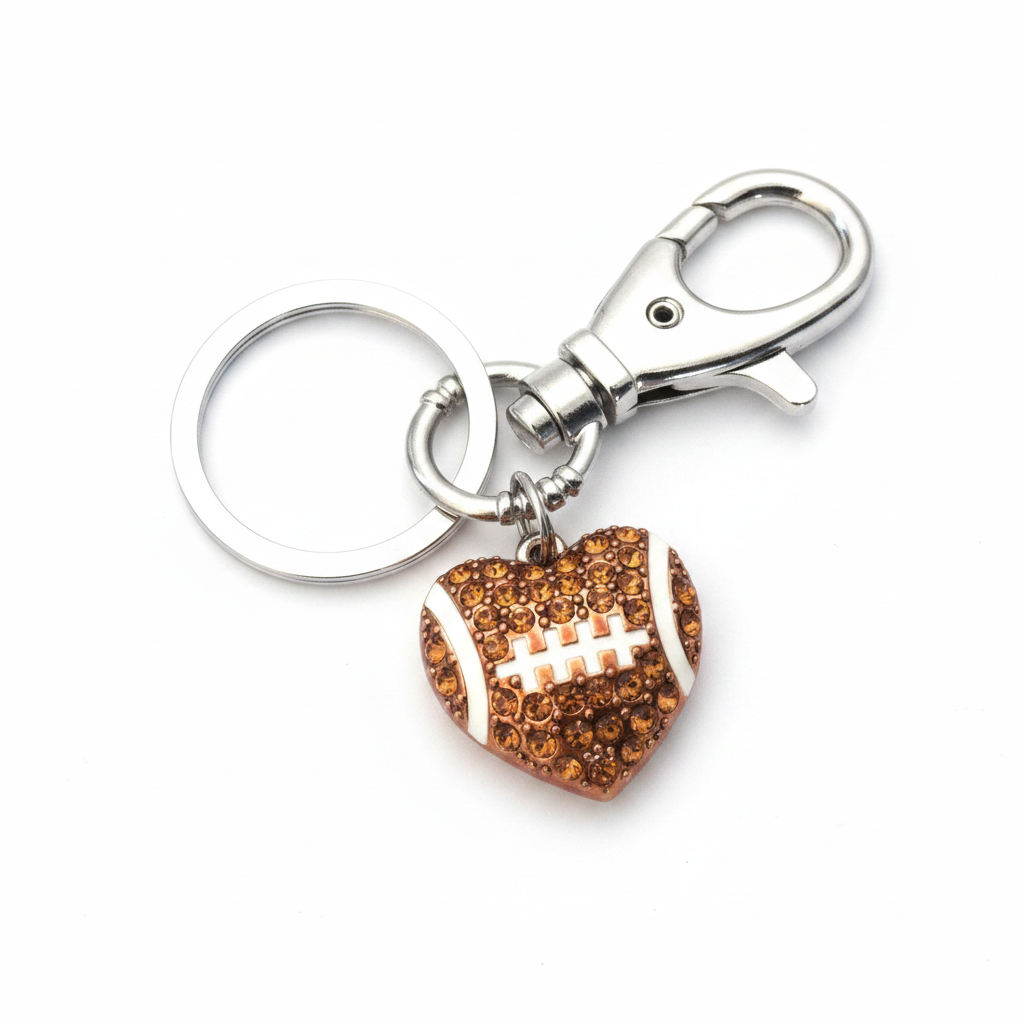 Crystal football heart keychain with amber faceted crystals and white enamel laces, attached to a silver swivel lobster clasp and split ring, photographed on a white studio background