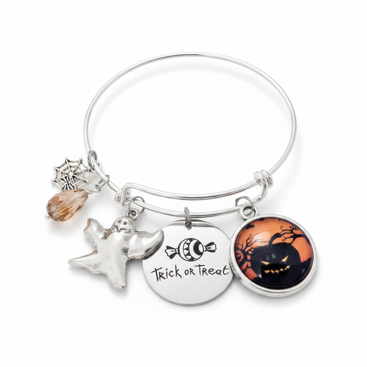 Silver expandable Halloween charm bangle bracelet on white background featuring spider web charm, amber crystal teardrop bead, ghost charm, Trick or Treat engraved disc charm, and jack-o-lantern glass cabochon pendant
