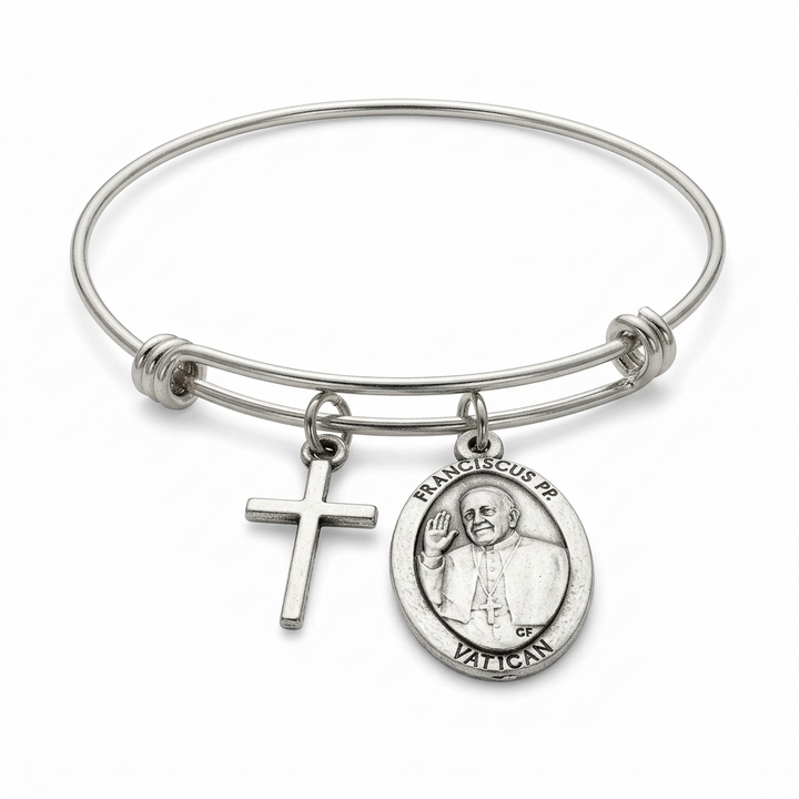 Expandable stainless steel bangle with attached cross charm and oval Pope Francis portrait medal on a white studio background.
