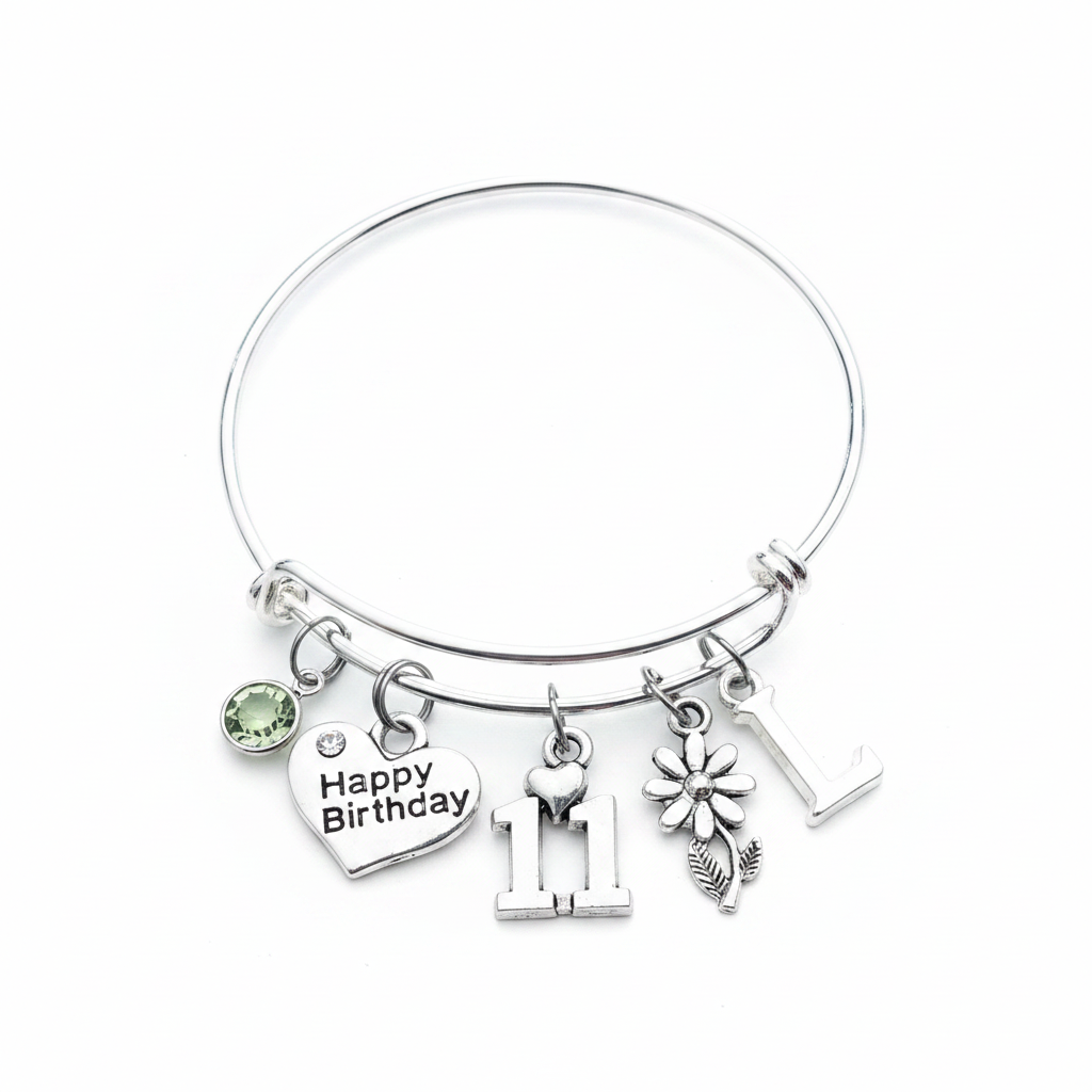 Silver expandable bangle bracelet with five charms: Happy Birthday heart charm with crystal, silver number 11 charm with tiny heart, silver daisy flower charm with stem and leaf, green peridot birthstone crystal charm, and silver letter initial charm — personalized adjustable stackable 11th birthday gift bracelet for girls