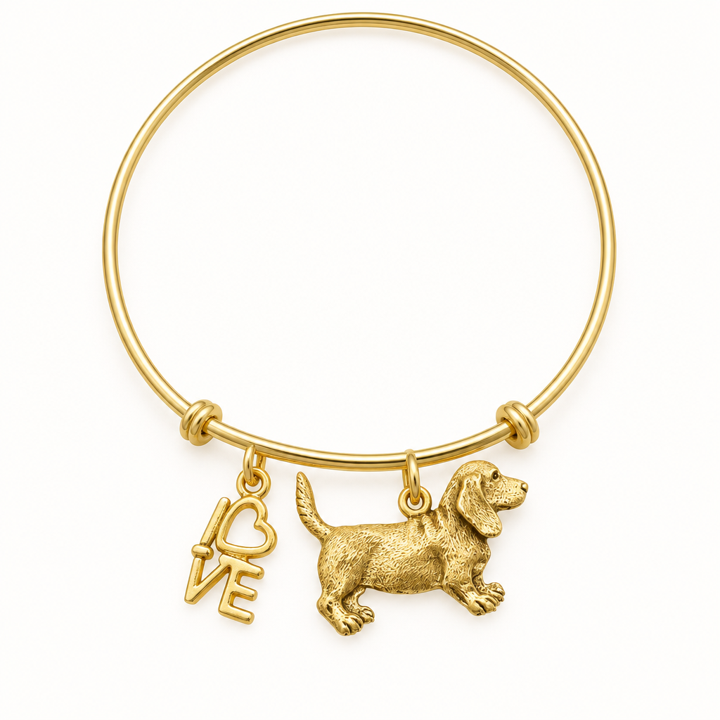 Gold bangle bracelet with a beagle dog charm and a LOVE script charm with a heart, shown on a warm-white studio background