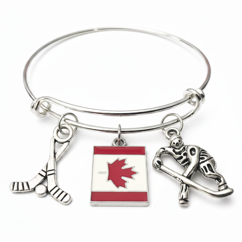 Silver expandable wire bangle bracelet with three charms each attached via individual jump rings: crossed hockey sticks with puck charm, red and white enamel Canadian flag maple leaf charm, and silver hockey player skating charm, evenly spaced on white background