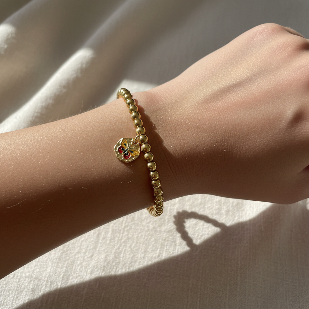 Woman wearing gold bead stretch bracelet with colorful enamel butterfly charm – dainty stacking jewelry by Jules Obsession