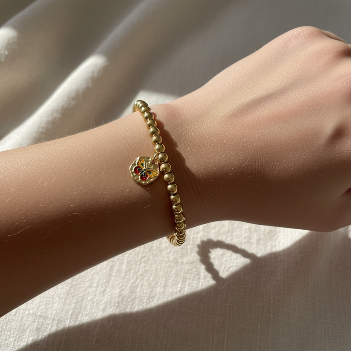 Woman wearing gold bead stretch bracelet with colorful enamel butterfly charm – dainty stacking jewelry by Jules Obsession