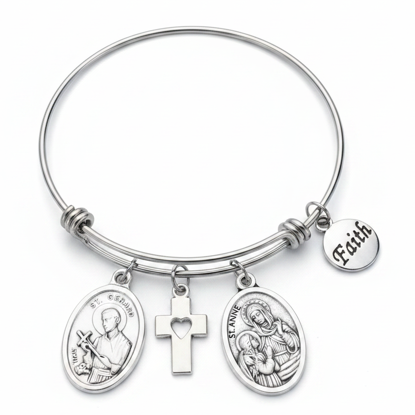 Silver stainless steel expandable bangle bracelet featuring St. Gerard and St. Anne oval medallion charms, a cross charm with heart cutout, and a round Faith disc charm, displayed on a white studio background