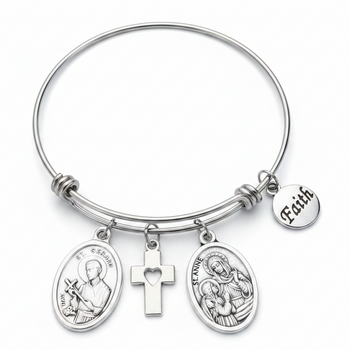 Silver stainless steel expandable bangle bracelet featuring St. Gerard and St. Anne oval medallion charms, a cross charm with heart cutout, and a round Faith disc charm, displayed on a white studio background