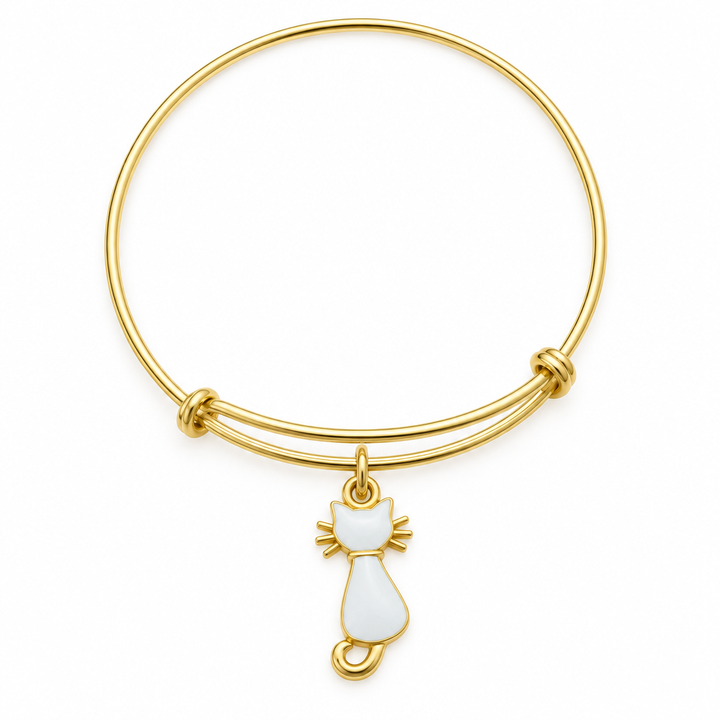 Gold bangle bracelet with a white resin cat-shaped charm with gold trim, shown on a warm-white studio background