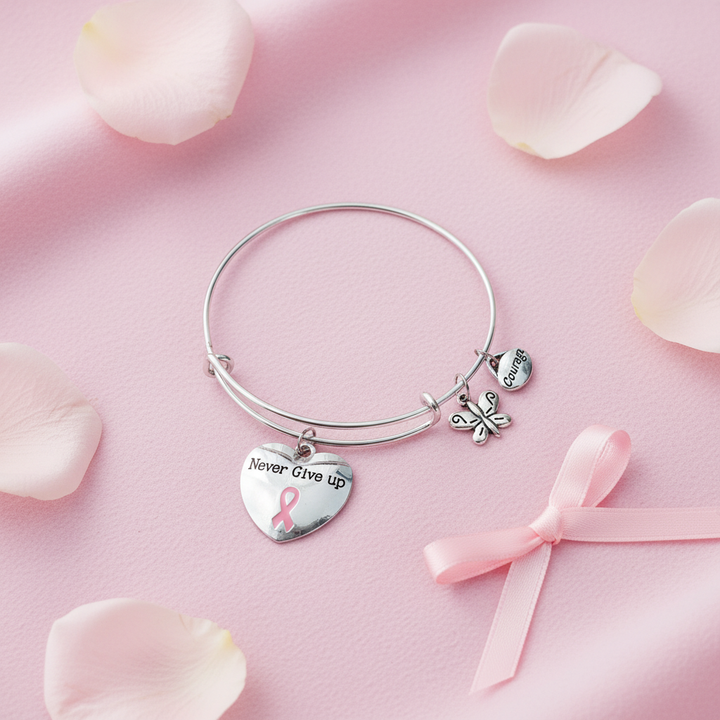Flat lay of silver pink ribbon Never Give Up charm bracelet on pink fabric with rose petals — breast cancer awareness jewelry gift by Jules Obsession