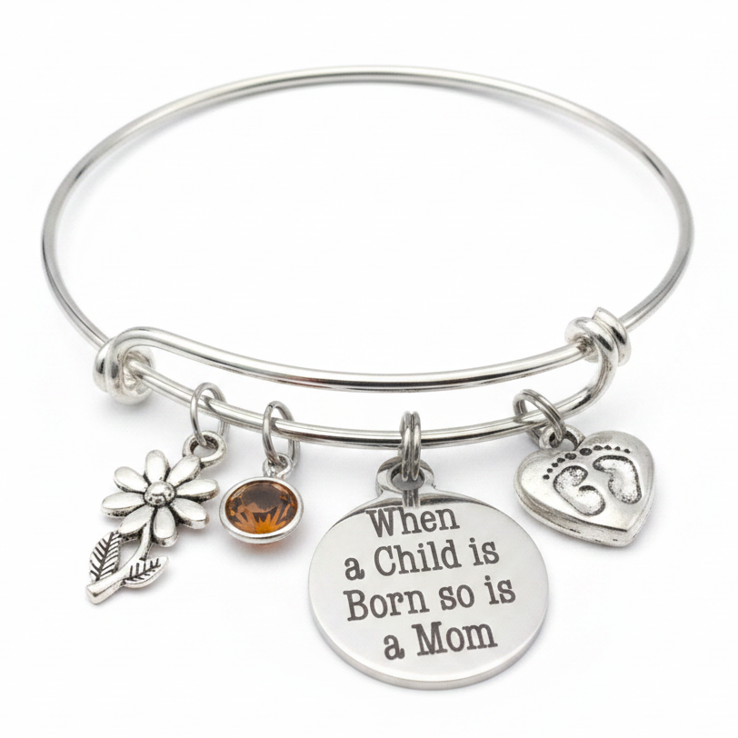 Silver expandable bangle bracelet with When a Child is Born So is a Mom disc charm, baby footprint heart charm, daisy flower charm, and amber birthstone crystal on white background – Jules Obsession new mom gift jewelry