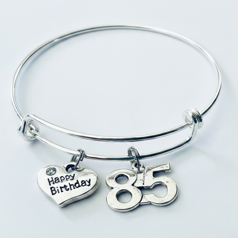 Polished silver expandable charm bangle bracelet with Happy Birthday heart charm featuring crystal accent and bold 85 number charm, displayed on white background — 85th birthday gift for women by Jules Obsession