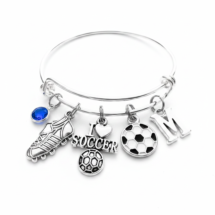 Silver expandable bangle bracelet with I Love Soccer charm, soccer cleat charm, enamel soccer ball charm, letter M initial charm, and royal blue birthstone charm on white background