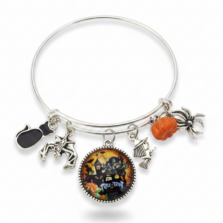 Silver expandable Halloween charm bangle bracelet on white background featuring black cat enamel charm, silver bat charm, Trick or Treat haunted house glass cabochon pendant, witch on broomstick charm, orange pumpkin bead, and silver spider charm