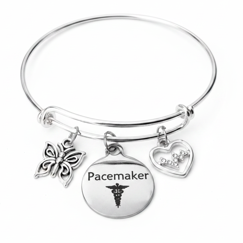 Silver expandable bangle bracelet with Pacemaker disc charm, crystal EKG heart charm, and butterfly charm on white studio background