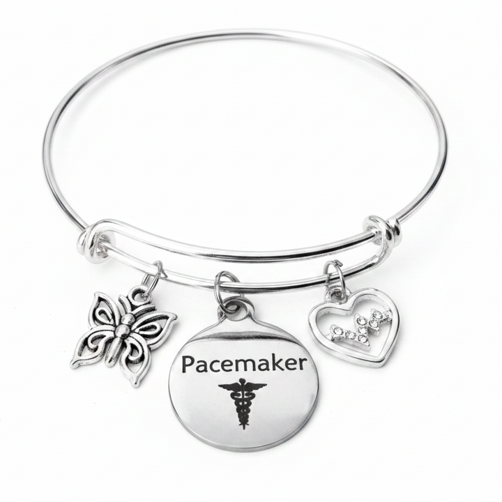 Silver expandable bangle bracelet with Pacemaker disc charm, crystal EKG heart charm, and butterfly charm on white studio background
