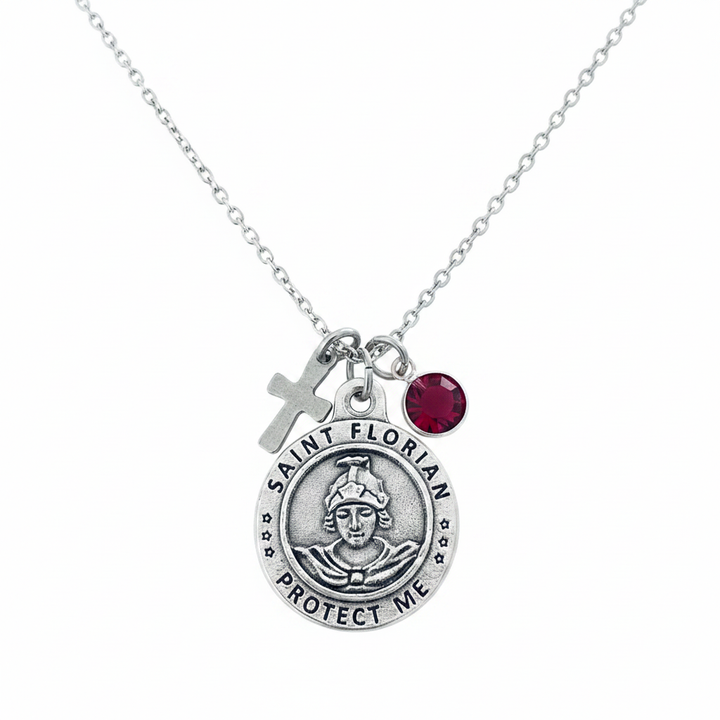 Saint Florian Protect Me silver medal charm necklace with small silver cross charm and ruby red faceted crystal birthstone on a delicate silver cable chain, white studio background