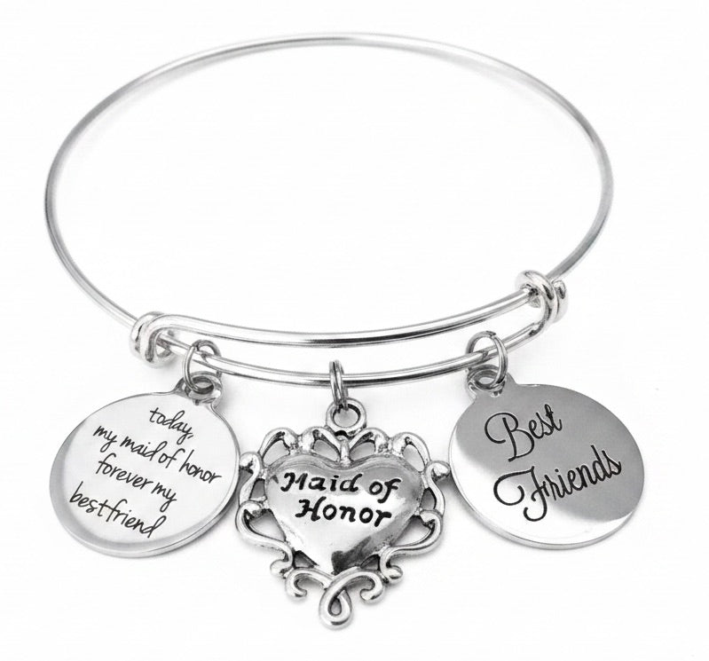 A silver-tone expandable bangle bracelet with three hanging charms: a heart-shaped ornament reading 'Maid of Honor,' and two round discs reading 'today my maid of honor forever my best friend' and 'Best Friends,' 