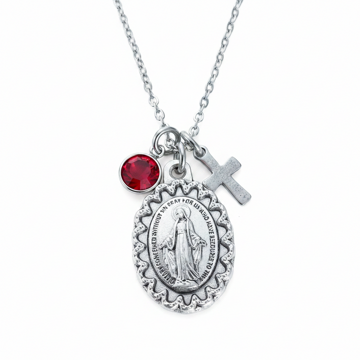 Oxidized silver Virgin Mary miraculous medal necklace on wood surface showing large oval scalloped medal, silver cross charm, and crystal birthstone charm on stainless steel cable chain