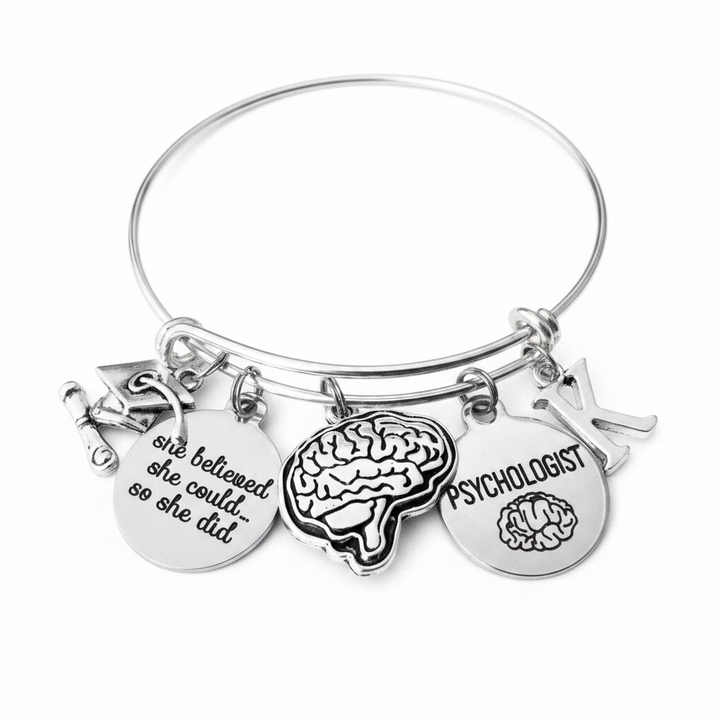 Psychologist graduation gift bracelet on white background — silver bangle with brain charm, she believed she could charm, Psychologist disc, and personalized initial charm