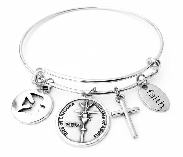 Silver expandable charm bangle bracelet with dove disc charm, RCIA Rite of Christian Initiation of Adults medallion charm, cross charm, and faith oval charm, handcrafted by Jules Obsession