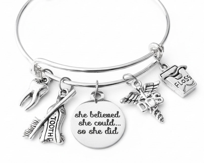 Silver expandable charm bangle bracelet with molar tooth, crossed toothbrush and toothpaste, She Believed She Could engraved disc, DDS caduceus, and dental floss charms — dental school graduation gift bracelet by Jules Obsession"