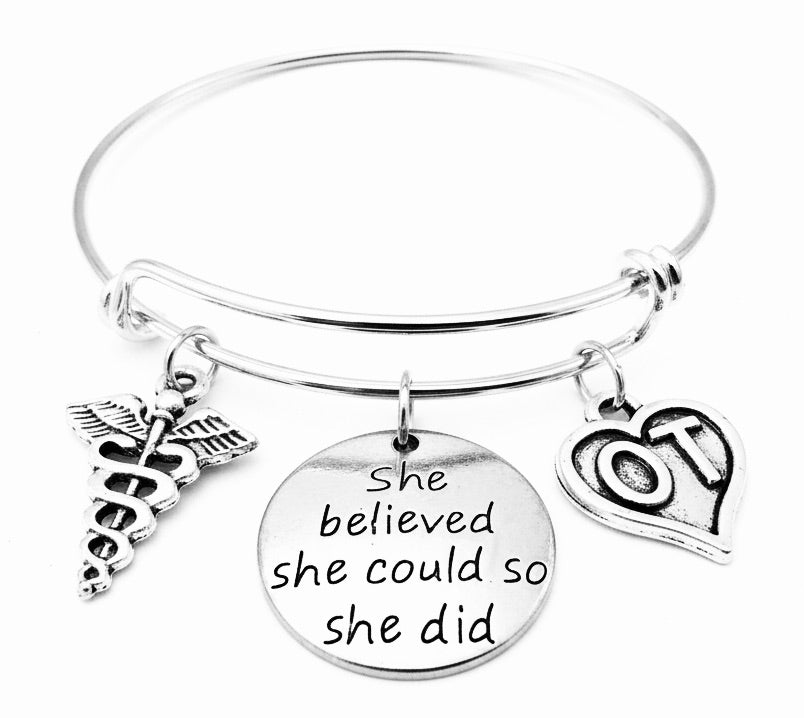 Silver expandable charm bangle bracelet with caduceus charm, She Believed She Could engraved disc, and OT heart charm — occupational therapist graduation gift bracelet by Jules Obsession