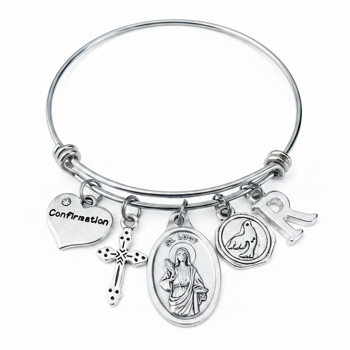 Confirmation charm bangle bracelet featuring Saint Lucy saint medal, decorative cross charm, Confirmation heart, Holy Spirit dove medallion, and personalized silver initial charm