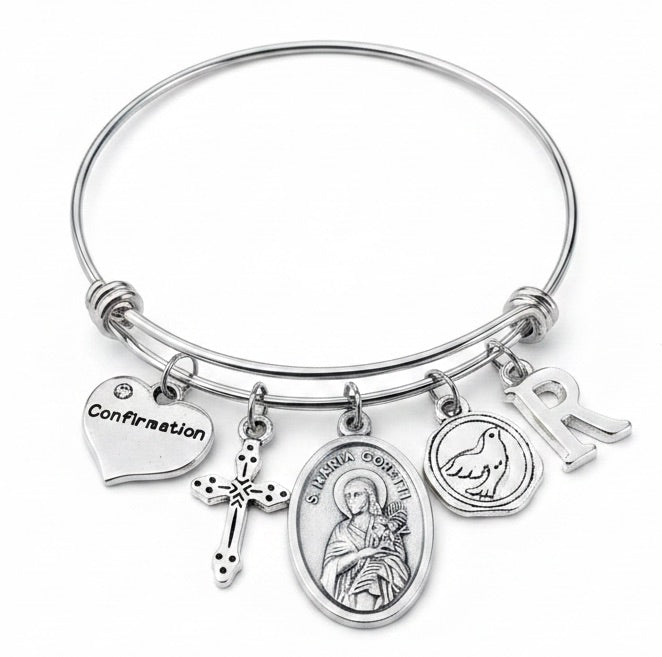 Confirmation charm bangle bracelet featuring St. Maria Goretti saint medal, decorative cross charm, Confirmation heart, Holy Spirit dove medallion, and personalized silver initial charm