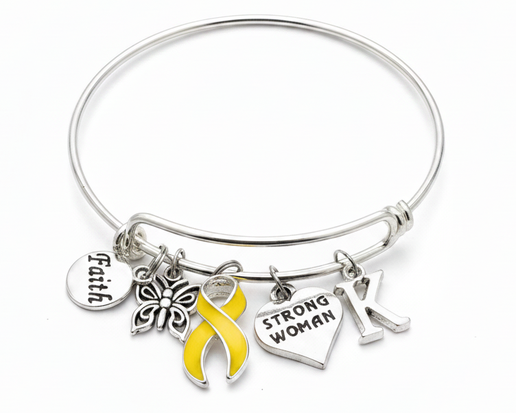 A silver-toned bangle bracelet with multiple charms, including a yellow awareness ribbon, a heart charm engraved &