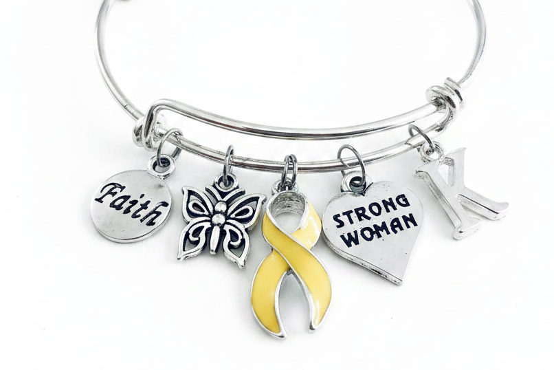 A silver-toned bangle bracelet with five charms, including a yellow awareness ribbon, a butterfly, a heart engraved &