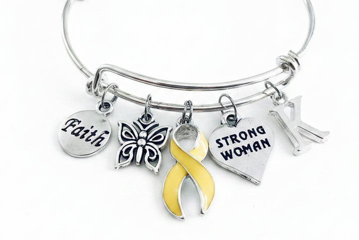 A silver-toned bangle bracelet with five charms, including a yellow awareness ribbon, a butterfly, a heart engraved &