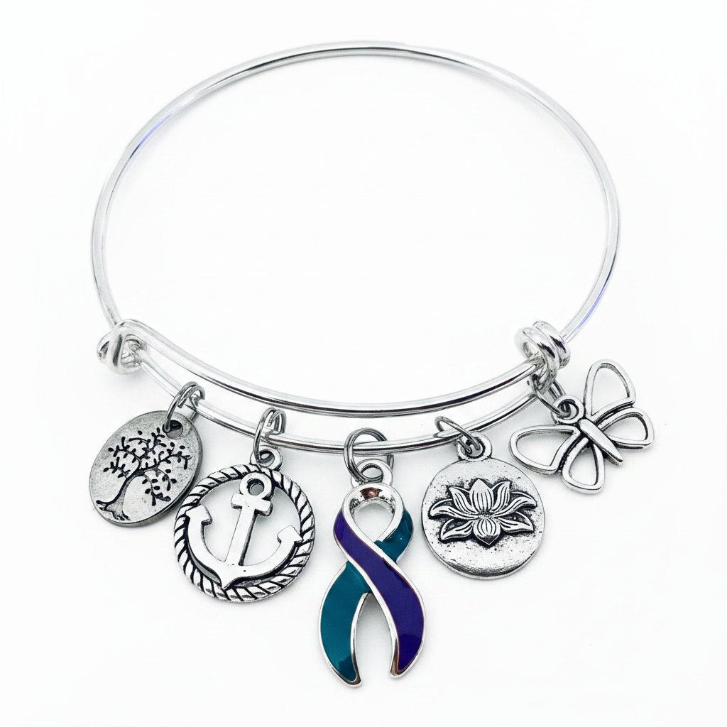 A silver-toned bangle bracelet with five dangling charms, including a tree, anchor, lotus flower, butterfly, and a teal-and-purple awareness ribbon, shown on a plain white background.