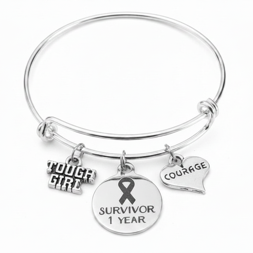 Silver expandable bangle bracelet with three charms: Tough Girl, a cancer awareness ribbon engraved Survivor 1 Year, and a heart engraved Courage — cancer survivor milestone gift