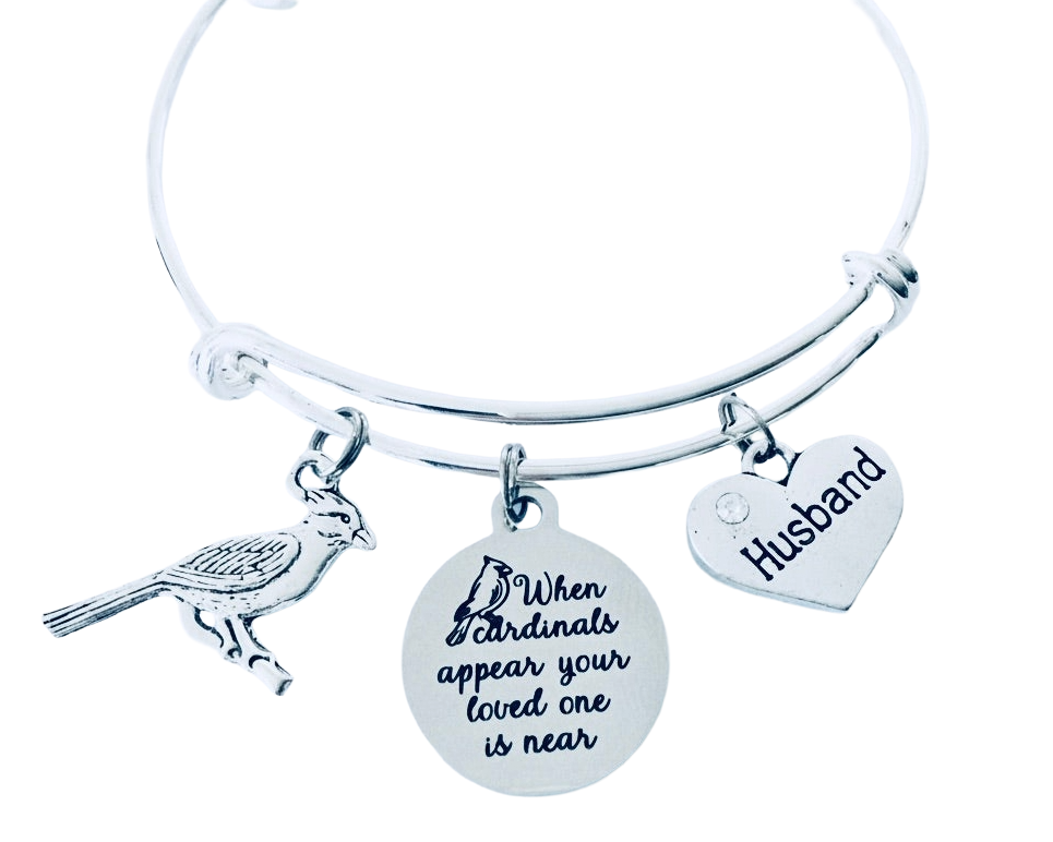 A silver-toned expandable bangle bracelet with three charms: a bird silhouette, a round disc engraved with &