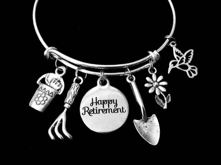 An expandable charm bracelet with silver adjustable bangle featuring gardening-themed charms such as a hummingbird, daisy, shovel, and flower, along with a &